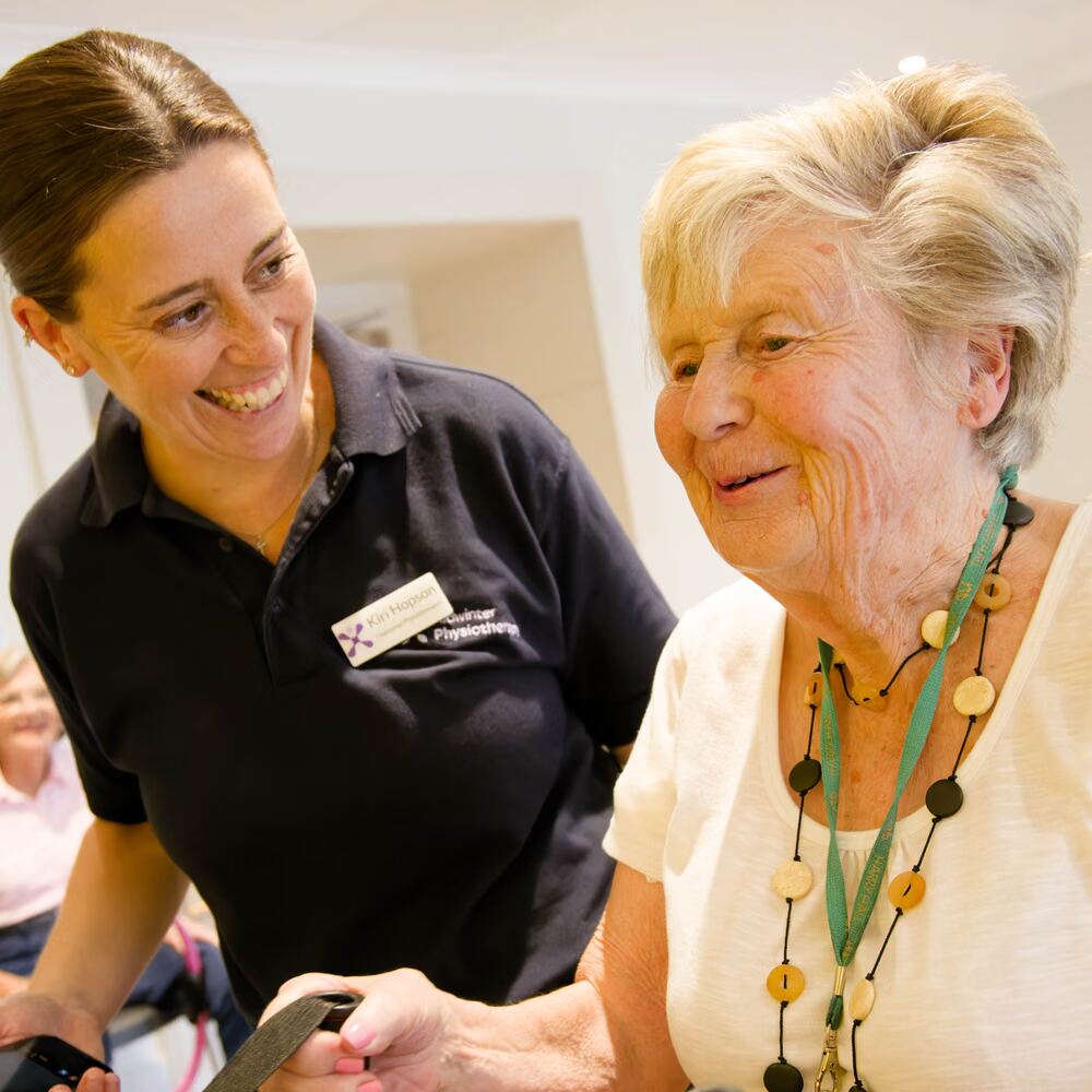 A physiotherapist supporting an older patient using resistance bands during a rehabilitation session.